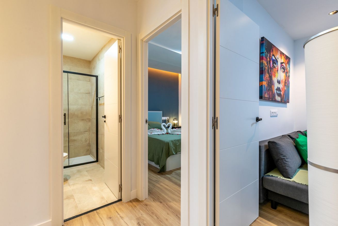 Een hotelkamer met een douchecabine van glas, een bed met een groene deken en een schilderij aan de muur.