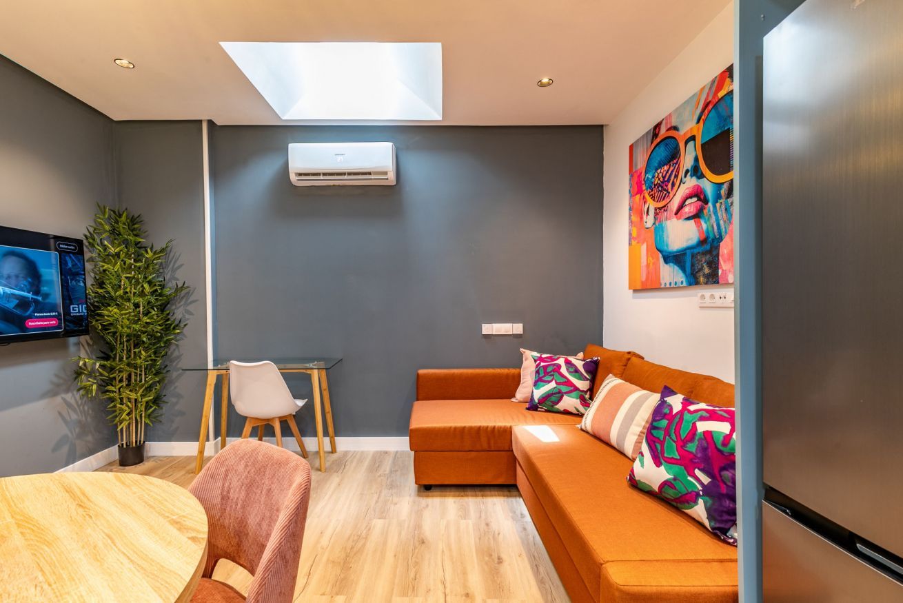 Una sala de estar moderna con un sofá, un televisor, una planta y un cuadro en la pared.