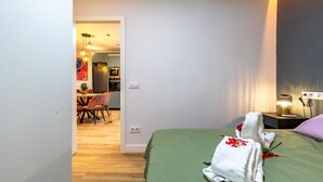 A hotel room with a green bed, a nightstand with a lamp, and a view of the dining area. - Spacious and modern 2-bedroom apartment – ​​Comillas (Madrid)