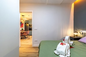 A hotel room with a green bed, a nightstand with a lamp, and a view of the dining area. - Spacious and modern 2-bedroom apartment – Comillas (Madrid)
