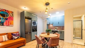 A modern kitchen with a central island, a dining area with a round table and chairs, and a shower room with glass doors. - Spacious and modern 2-bedroom apartment – ​​Comillas (Madrid)