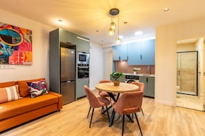 A modern kitchen with a central island, a dining area with a round table and chairs, and a shower room with glass doors. - Spacious and modern 2-bedroom apartment – Comillas (Madrid)