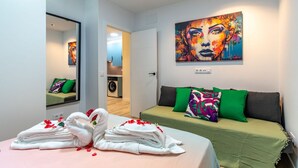 A hotel room with a bed, a green sofa, a painting on the wall, and a washing machine in the background. - Spacious and modern 2-bedroom apartment – ​​Comillas (Madrid)