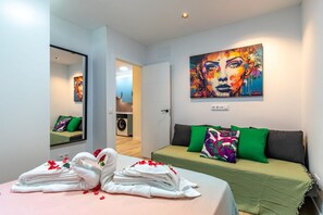 A hotel room with a bed, a green sofa, a painting on the wall, and a washing machine in the background. - Spacious and modern 2-bedroom apartment – Comillas (Madrid)