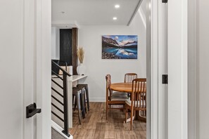 A dining area with a wooden table and chairs, a painting of a mountain landscape, and a staircase leading to an upper level. - Mountain Views | Outdoor Heated Pool | Hot Tub (Canmore)