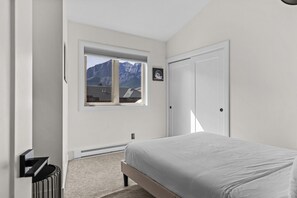 A bedroom with a bed, a window with a mountain view, a door, and a radiator. - Mountain Views | Outdoor Heated Pool | Hot Tub (Canmore)