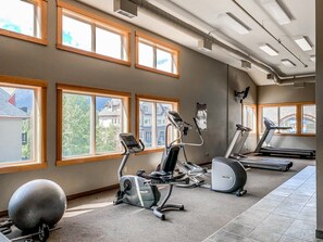 A gym with exercise equipment, large windows, and a view of buildings outside. - Mountain Views | Outdoor Heated Pool | Hot Tub (Canmore)