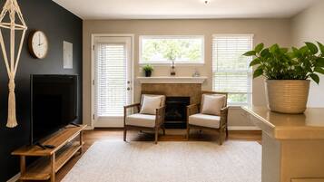A living room with a fireplace, two armchairs, a TV, and a large potted plant.