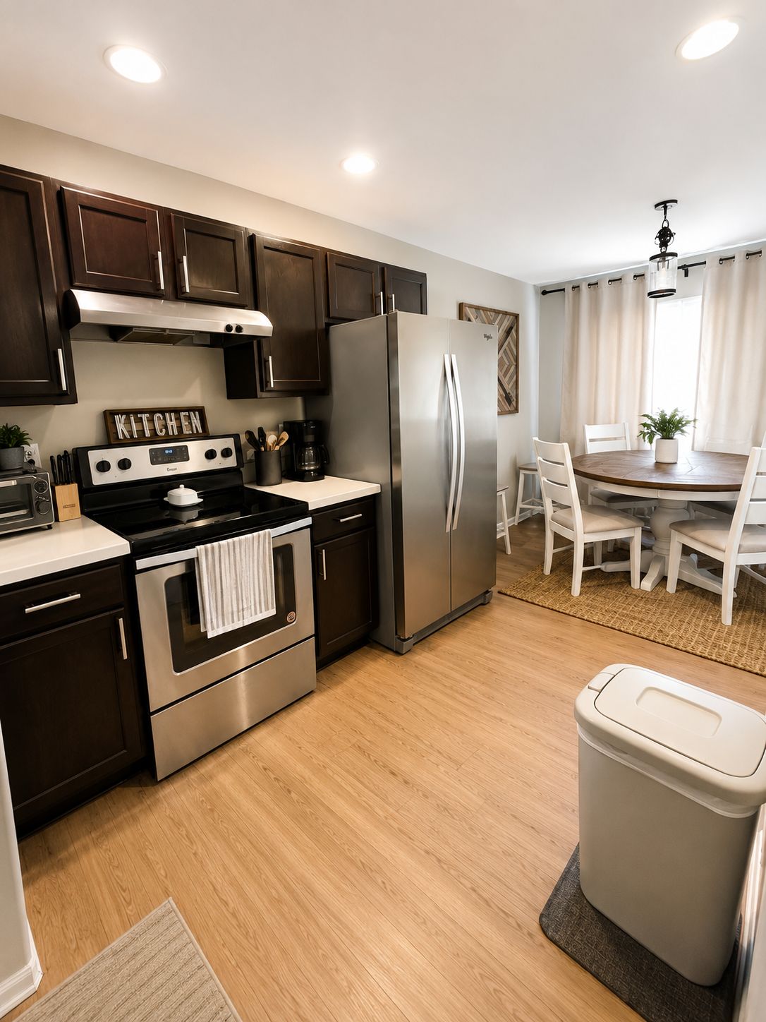 A modern kitchen with stainless steel appliances, a dining area with a round table, and a trash bin.