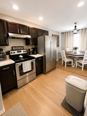 A modern kitchen with stainless steel appliances, a dining area with a round table, and a trash bin.