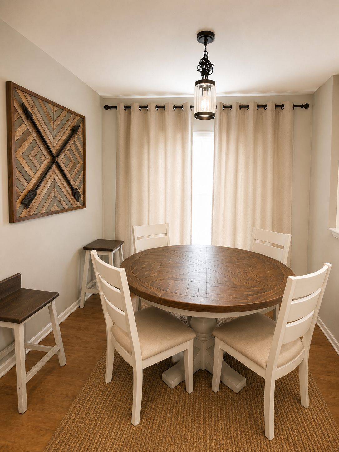 A dining area with a round wooden table surrounded by white chairs, a woven rug, and a pendant light.