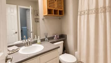 A bathroom with a double sink, a toilet, a wooden cabinet, a shower curtain, and a mirror.
