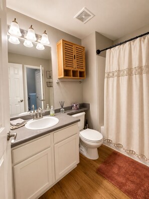 Un baño con lavamanos doble, inodoro, armario de madera, cortina de ducha y espejo.