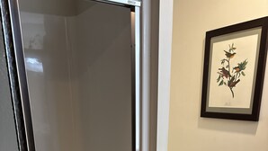 Un baño con cabina de ducha de vidrio, un inodoro y una obra de arte enmarcada en la pared.