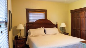 Un dormitorio con cama, dos mesitas de noche con lámparas, una ventana con persianas y un armario.