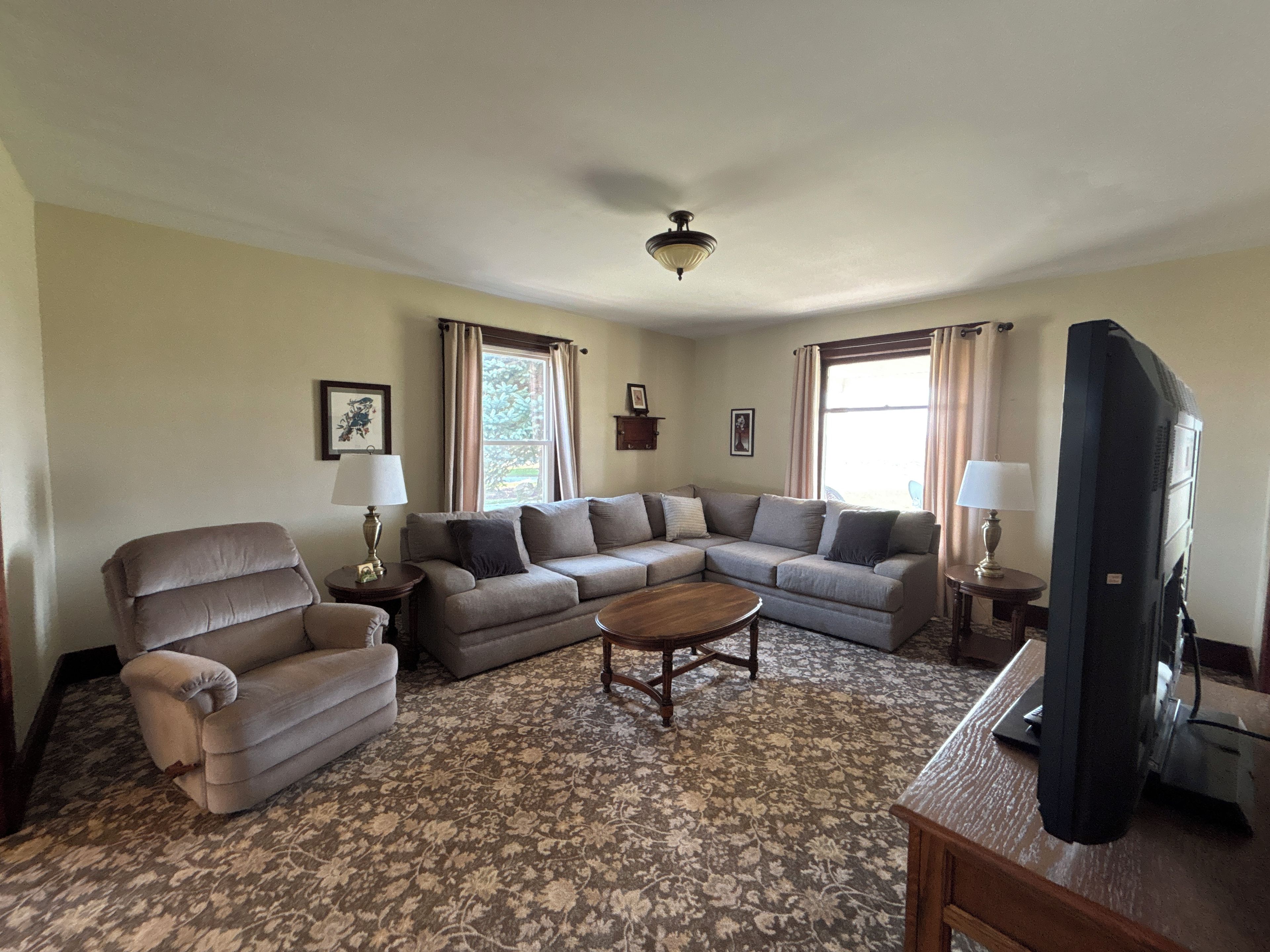 A living room with a sectional sofa, a recliner, a coffee table, a television, and a patterned carpet.