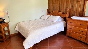Un dormitorio con cama, cabecera de madera, mesita de noche, lámpara y cómoda.