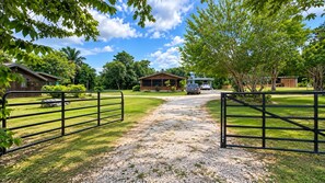 A gravel driveway leading to a gated entrance with a vehicle parked in the distance.