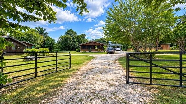 A gravel driveway leading to a gated entrance with a vehicle parked in the distance.