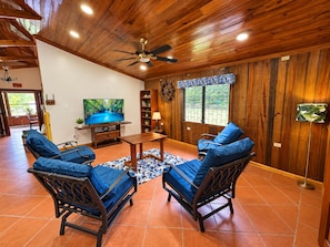 A room with wooden walls and ceiling, a television, two blue cushioned chairs, a small table, and a patterned rug.