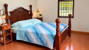 Un dormitorio con cama de madera con dosel, una mesita de noche con lámpara y una ventana con vista a zonas verdes.