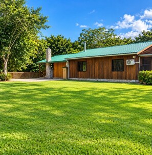 A wooden building with a green roof, a stone chimney, and a well-maintained lawn.