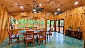 Un intérieur en bois comprenant un coin repas, des ventilateurs de plafond et de grandes fenêtres.