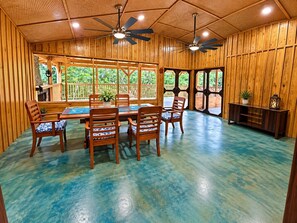 Un interior de madera con comedor, ventiladores de techo y ventanas amplias.