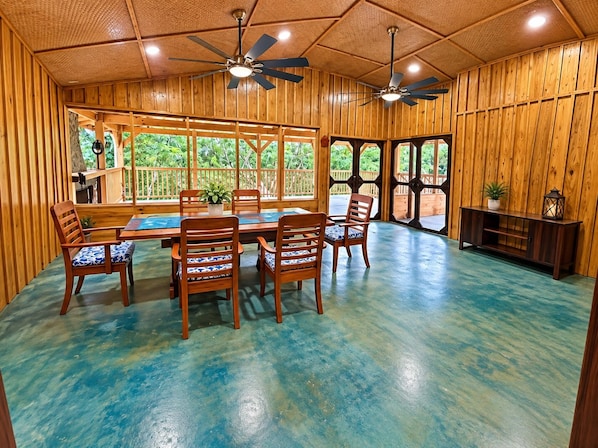 A wooden interior with a dining area, ceiling fans, and large windows.