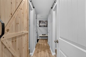 A narrow hallway with wooden doors on one side and white doors on the other, leading to a room with a bench and a poster on the wall. - Beautiful 5-bedroom house with all the amenities and convenient location. (Ellenwood)