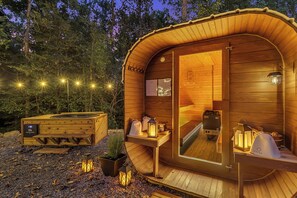En træhytte med spejlbeglasede vægge, sauna og et lille udendørs siddeområde.