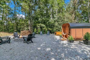 Et hyggeligt udendørs opholdsområde med bålsted, Adirondack-stole og en trækonstruktion.