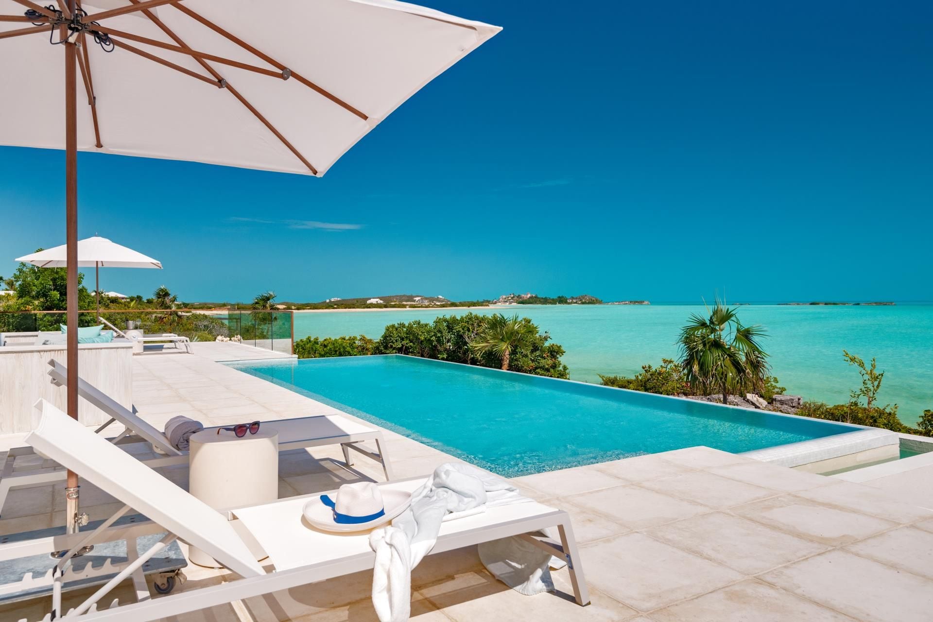 Un espace aménagé au bord de la piscine, avec des chaises longues, un parasol et une vue sur l’océan.