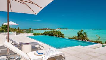 Un espace aménagé au bord de la piscine, avec des chaises longues, un parasol et une vue sur l’océan.