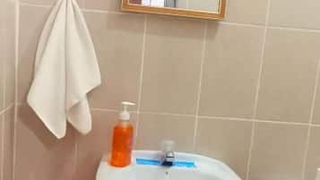 Une salle de bain avec un lavabo sur colonne, une serviette blanche accrochée au mur, un miroir et une poubelle noire.