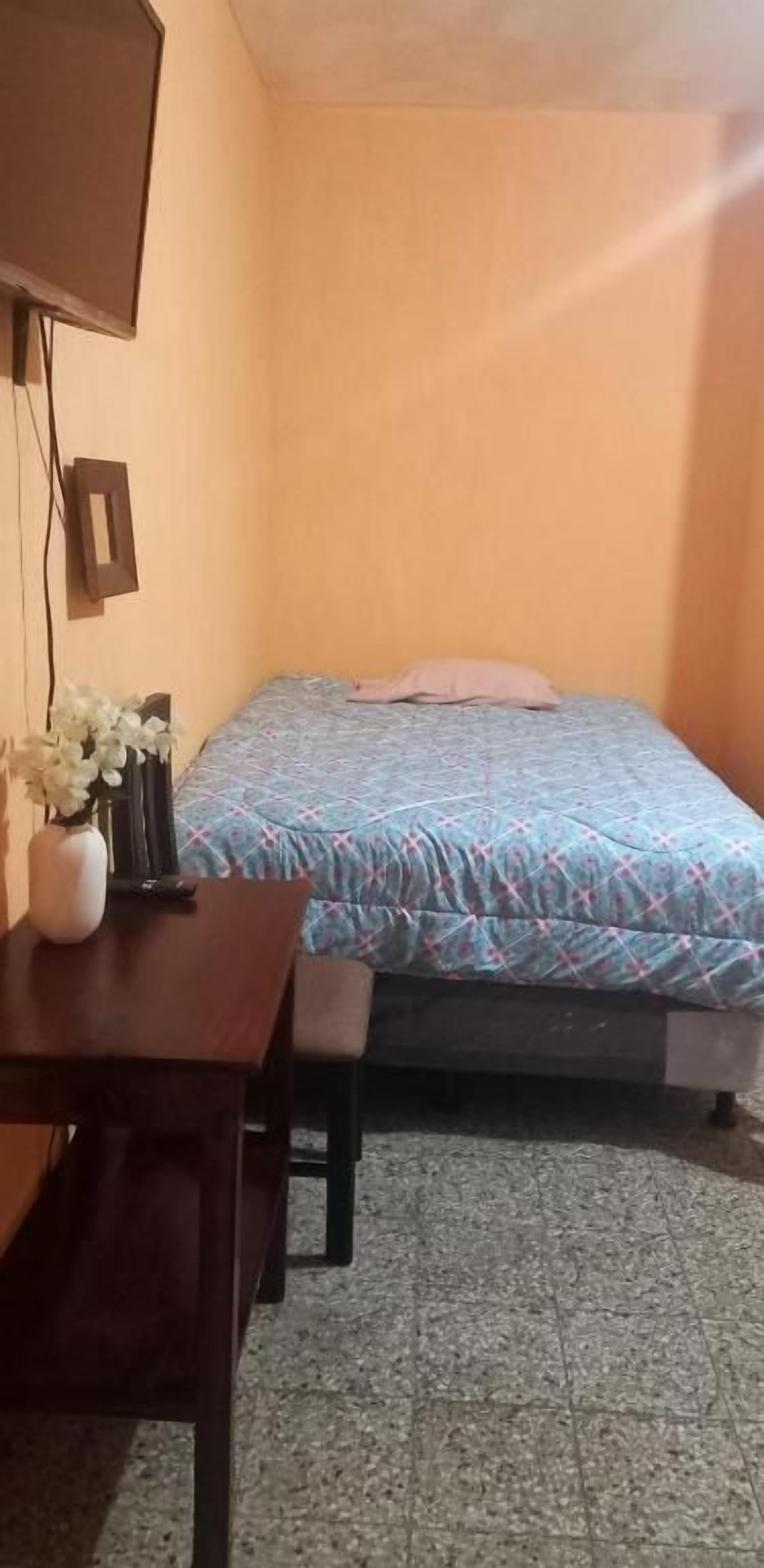 Una habitación pequeña con una cama, un escritorio y un televisor en la pared.