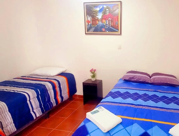 A room with two beds, a painting on the wall, and a small table with a flower. - Hotel Maya America (Panajachel)
