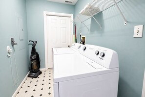 A laundry room with a front-loading washer and dryer, a vacuum cleaner, and a drying rack. - Parrot Bay Townhouse 27 | Pet Friendly (Ocean City)