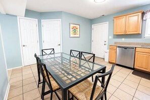 A dining area with a glass-top table and black chairs, surrounded by light blue walls and white doors. - Parrot Bay Townhouse 27 | Pet Friendly (Ocean City)