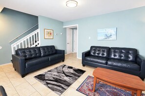 A living room with two black leather sofas, a wooden coffee table, and a patterned rug. - Parrot Bay Townhouse 27 | Pet Friendly (Ocean City)