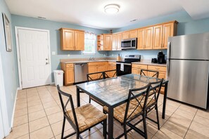 A compact kitchen with wooden cabinets, a stainless steel refrigerator, a microwave, and a glass dining table with chairs. - Parrot Bay Townhouse 27 | Pet Friendly (Ocean City)