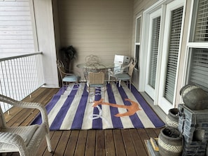A covered porch with wicker furniture, a striped rug, and potted plants.