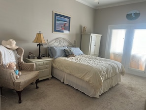A bedroom with a bed, nightstand, lamp, chair, and a framed picture on the wall.