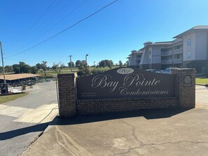 A sign for Bay Pointe Condominiums with a clear view of the parking lot and a building in the background.