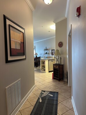 A hallway with a framed abstract painting, a kitchen area with a dishwasher, and a dining area with chairs.