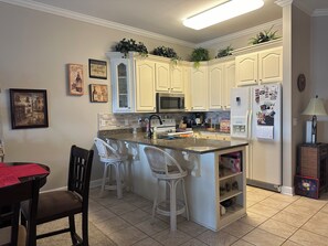 A kitchen with white cabinets, a granite countertop, a refrigerator, and bar stools.