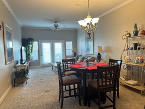 A dining area with a chandelier, a table set with red placemats, and a view of the living room through a doorway.