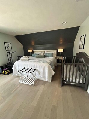 Ein Schlafzimmer mit Bett, Nachttischen, einem Kinderbett, einem Standventilator und Trainingsgeräten.