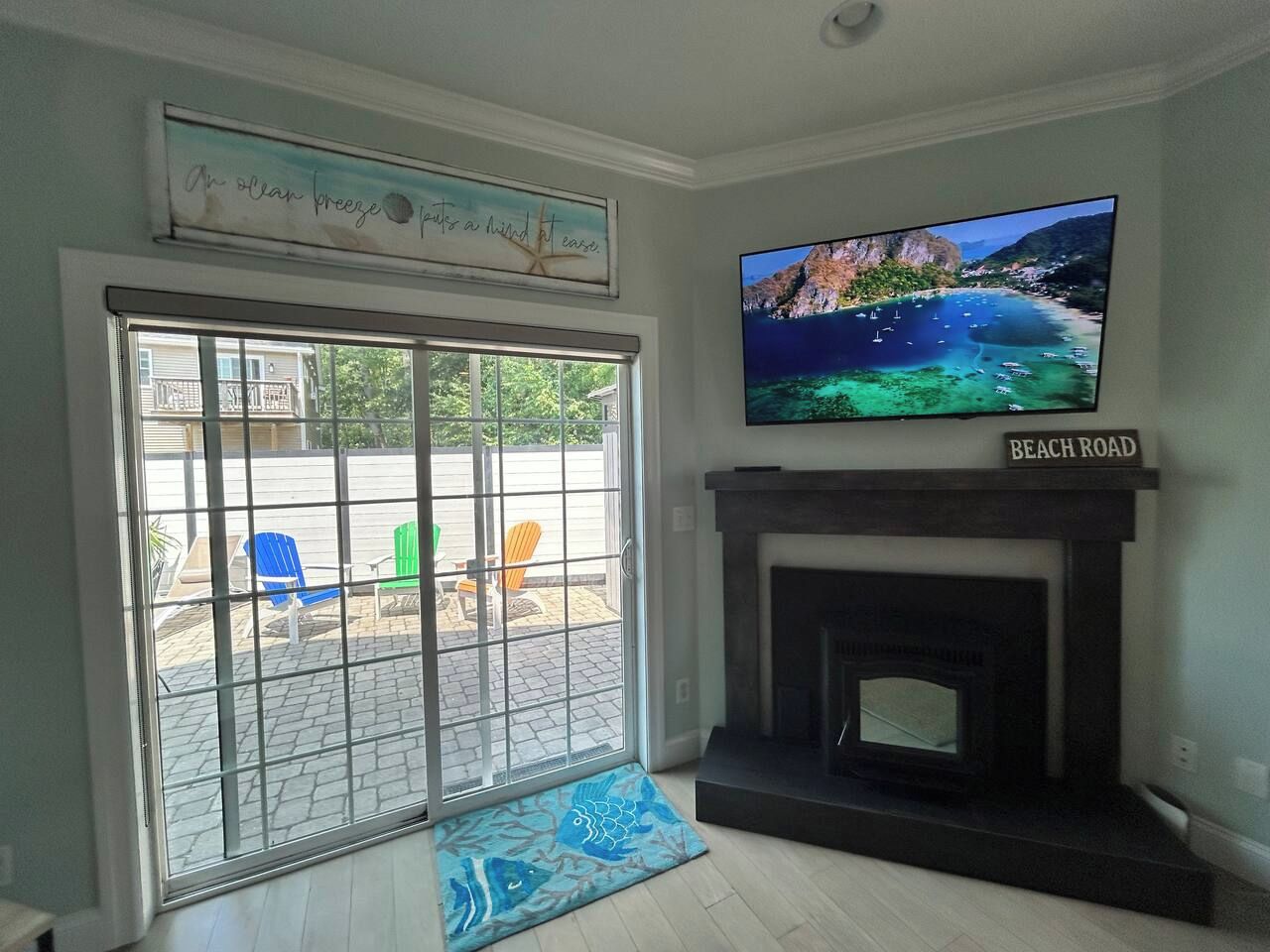 Sala de estar com lareira, televisão montada acima e vista para a praia através de uma porta de vidro deslizante.