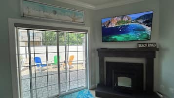 Sala de estar com lareira, televisão montada acima e vista para a praia através de uma porta de vidro deslizante.